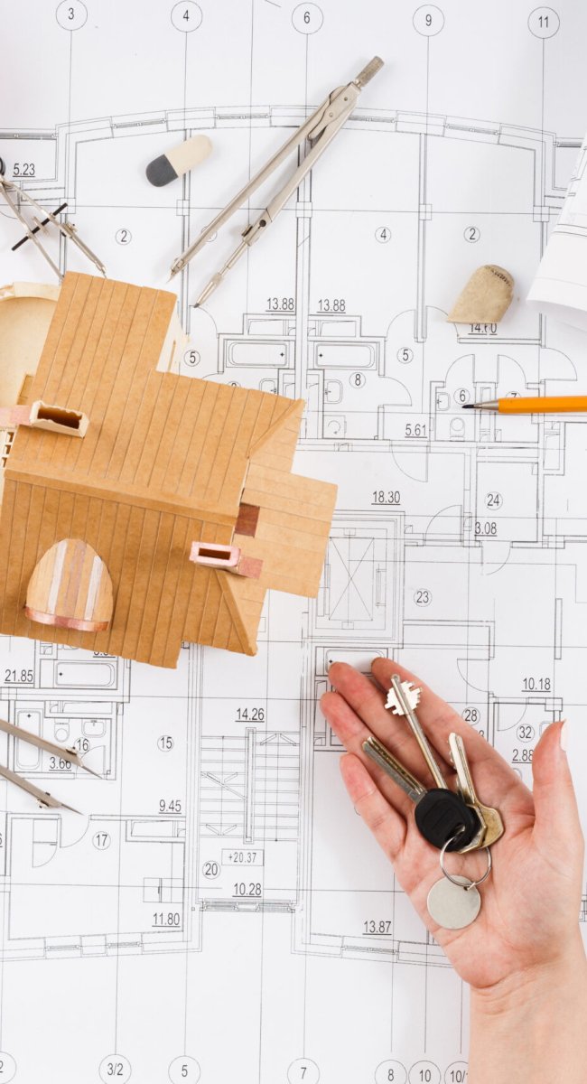 Architect holding keys at wooden house model in office, top view. Designer working with new project, copy space